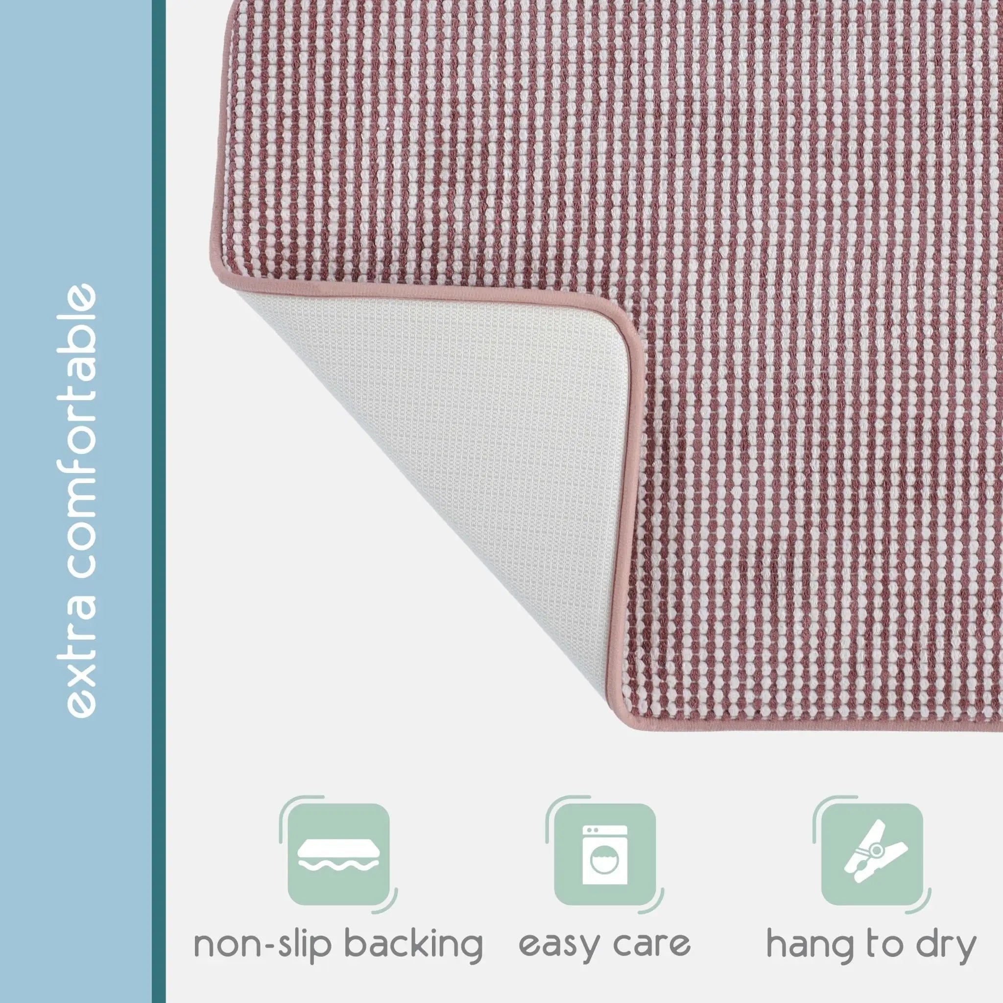A close-up of a rectangular berry color bath rug. A vertical blue-gray sidebar reads 'extra comfortable,' and three pale green icons at the bottom indicate non-slip backing, easy care, and hang-to-dry capability.