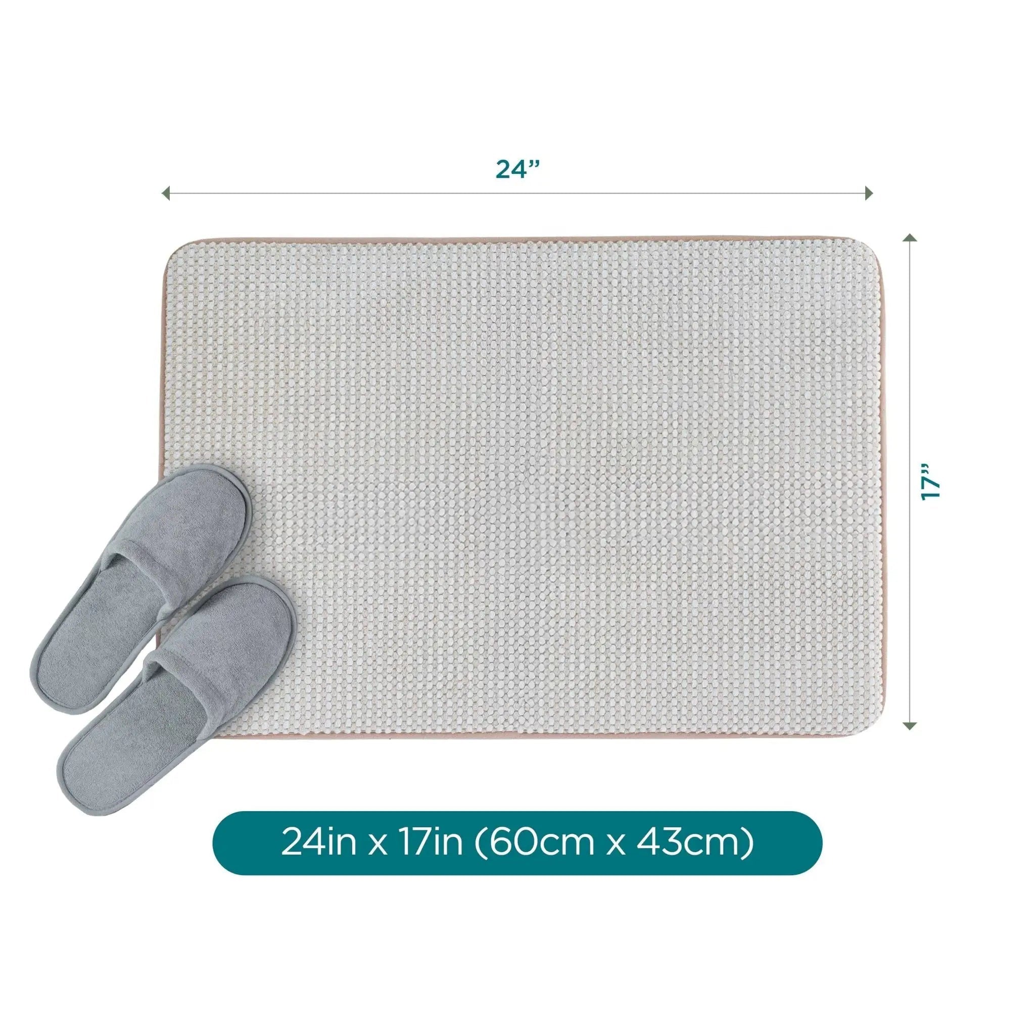 A rectangular sand color bath rug shown on a white background with dimension arrows indicating 24 inches by 17 inches, plus a pair of gray slippers placed on the mat and a teal label at the bottom reading 24in x 17in (60cm x 43cm).