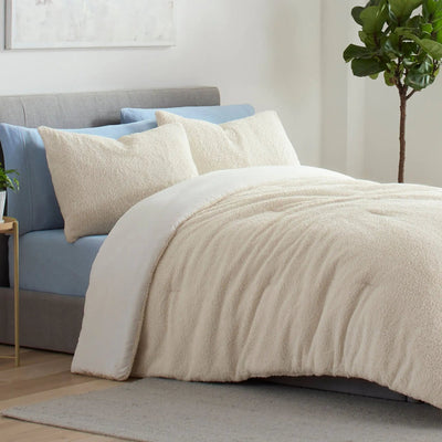 A cozy bed setup in a bright bedroom featuring a beige comforter, matching beige pillows shams, and light blue sheets.