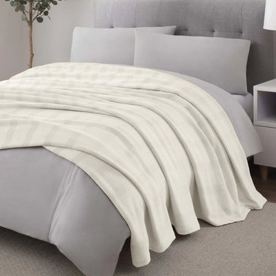 Gray bed with ivory blanket and pillows in a bedroom setting