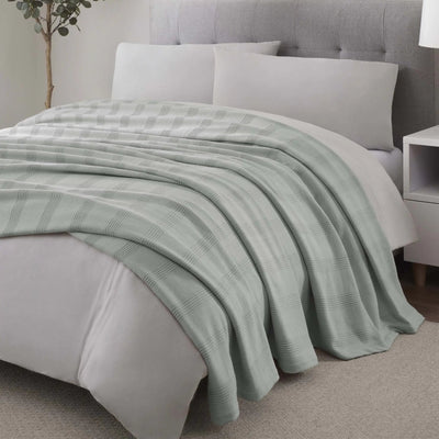 A grey textured throw blanket with a subtle striped pattern draped over a bed with white linens.