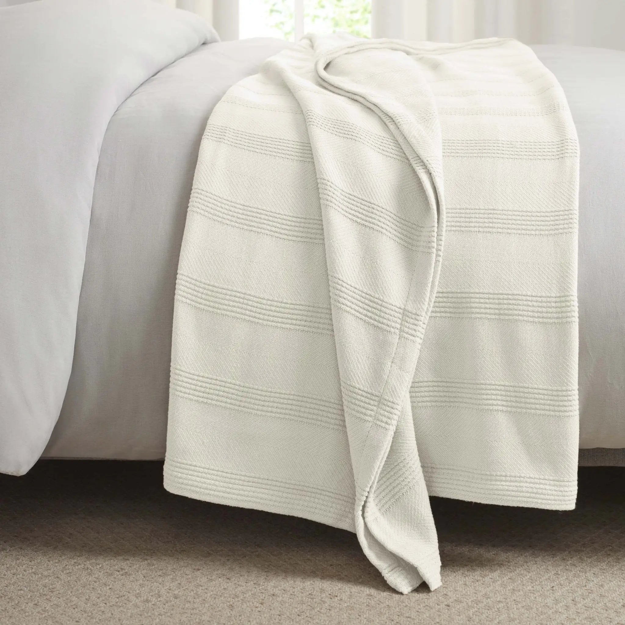 Ivory textured blanket draped over a bed with white bedding.
