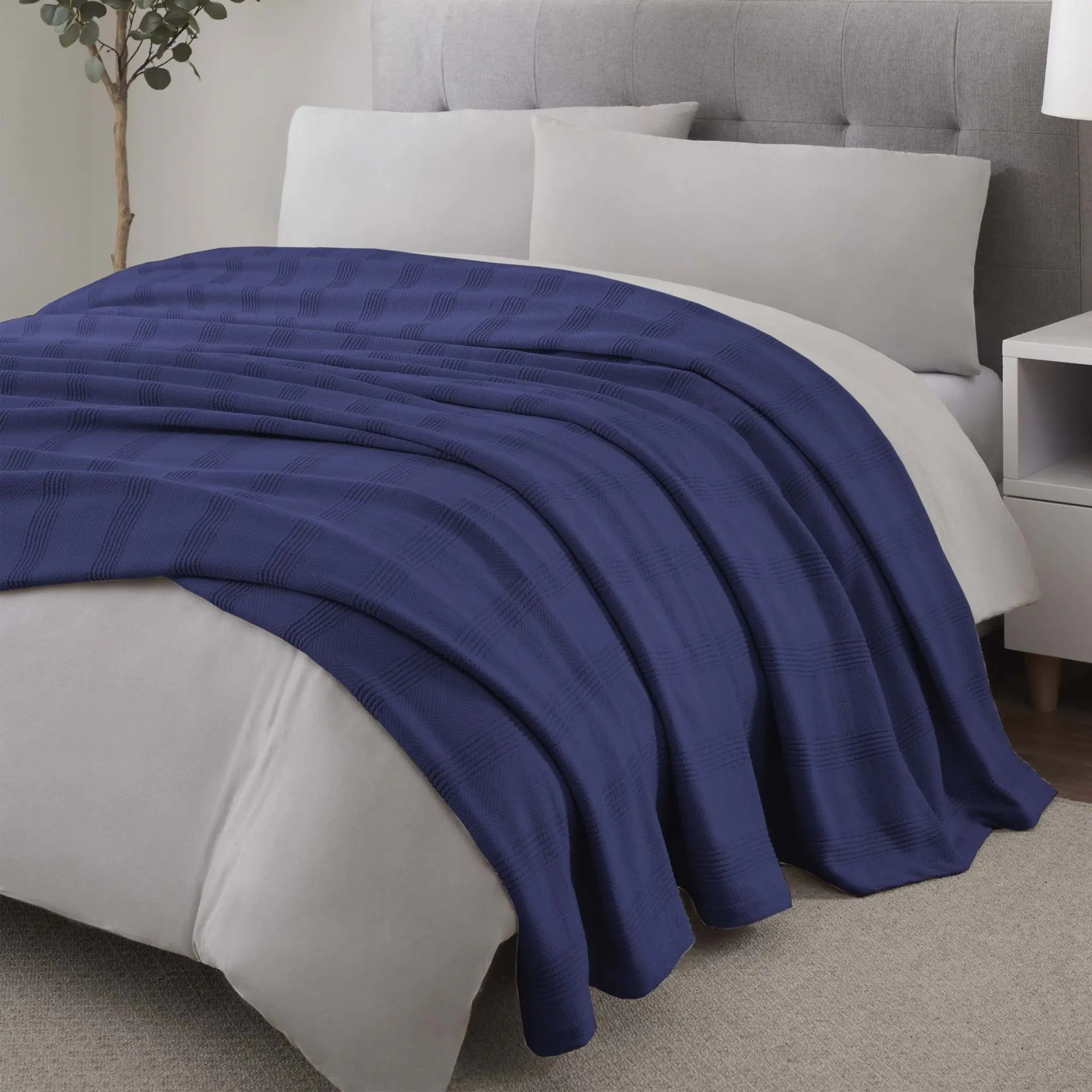 Navy blanket draped over a bed with gray bedding and headboard.