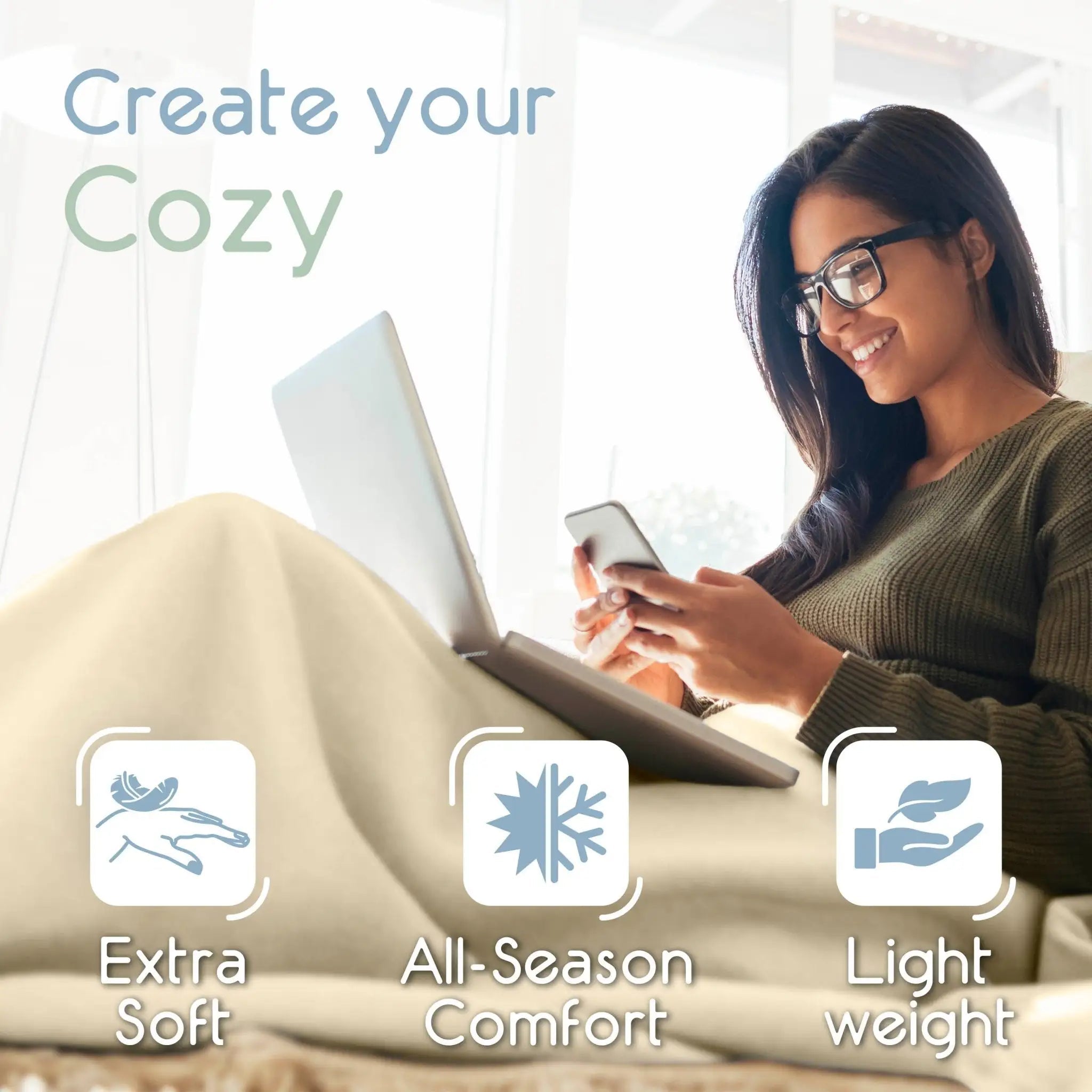 Woman using a laptop and phone on a Winter white blanket with text 'Create your Cozy' and icons for extra soft, all-season comfort, and light weight.