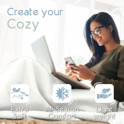 A woman wearing glasses reclines on a star white blanket with a laptop and phone, under the text 'Create your Cozy' and feature icons for 'Extra Soft', 'All-Season Comfort', and 'Light weight'.