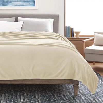 Winter white blanket on a bed in a bedroom setting with books and a chair.