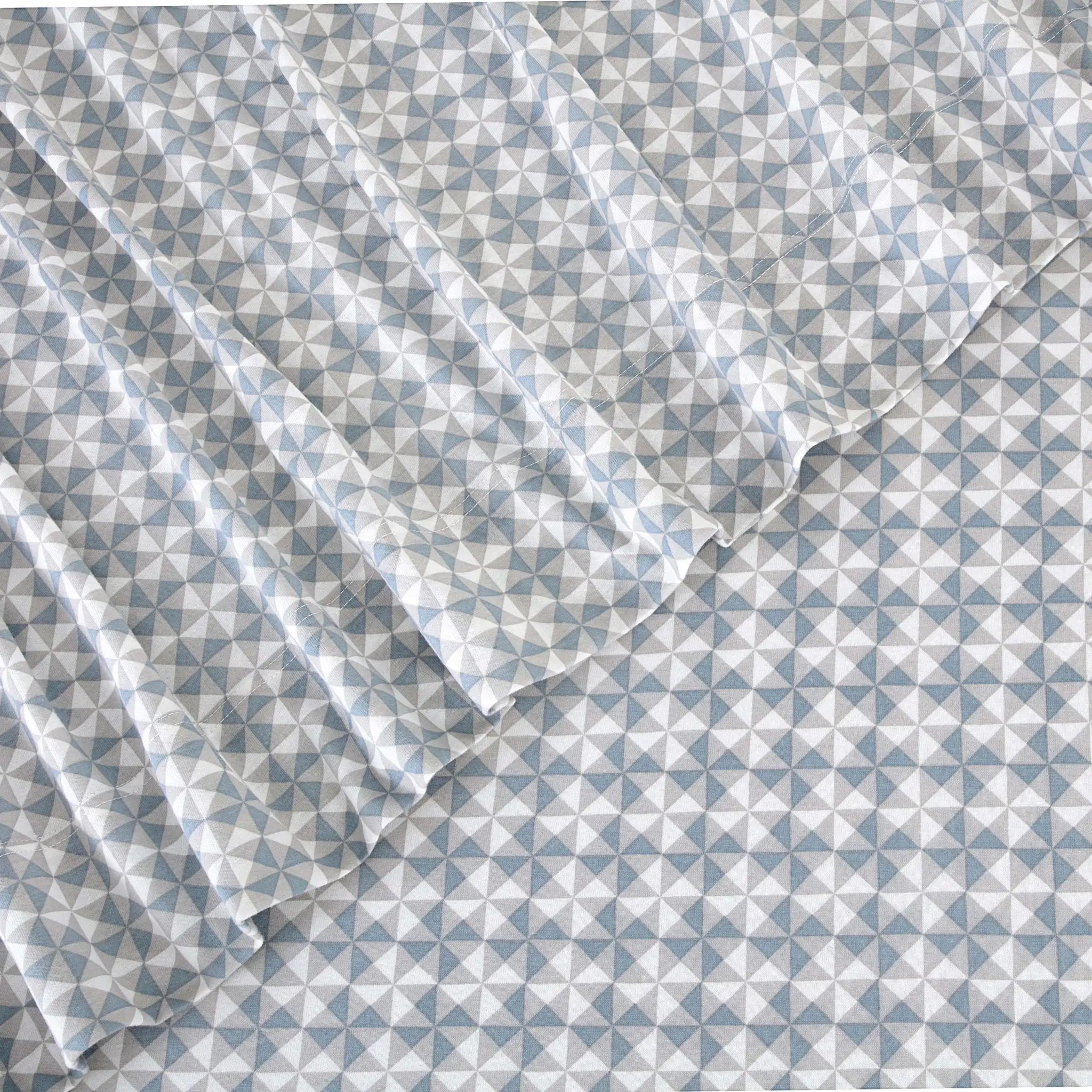 A close-up of a white fabric with a repeating geometric triangle pattern in light blue, shown with soft folds.