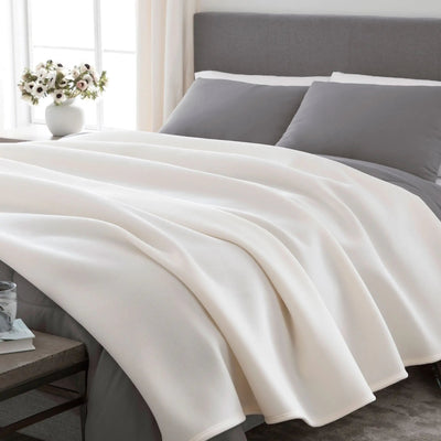 Ivory blanket on a bed with gray pillows.