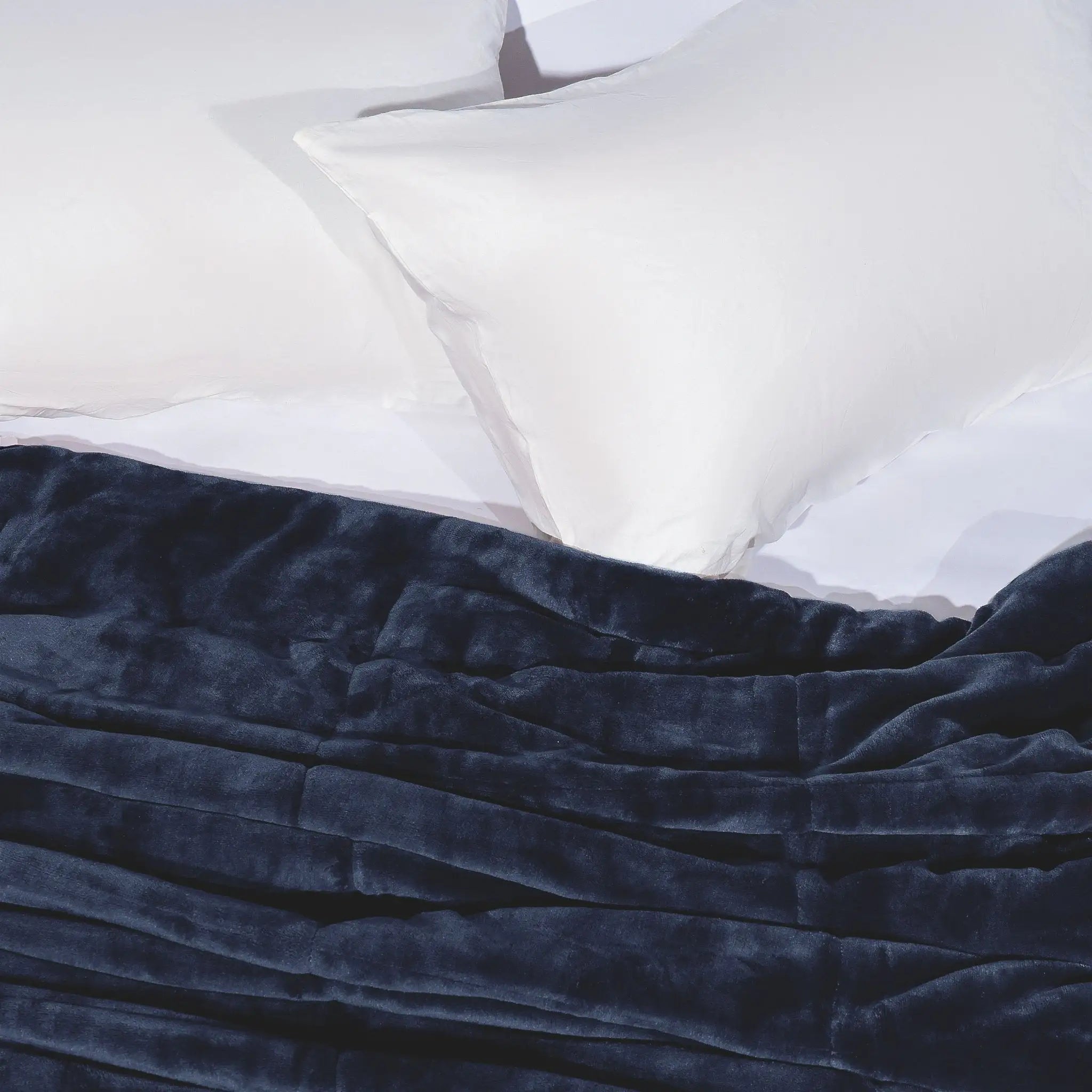 Blue blanket draped over a bed with white pillows