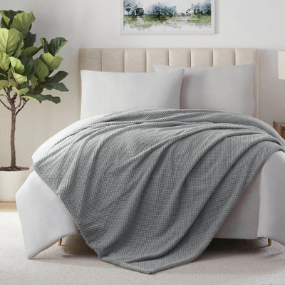 Gray textured blanket draped over a bed in a bedroom setting.
