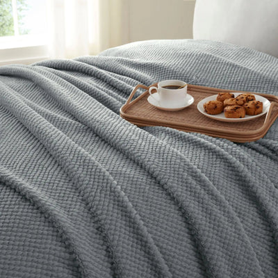 Gray textured blanket draped over a bed.