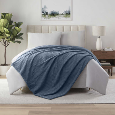 Blue textured blanket draped over a bed in a bedroom 
