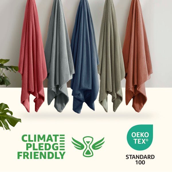 Five colorful towels hanging against a white wall with Climate Pledge Friendly and OEKO-TEX Standard 100 logos.