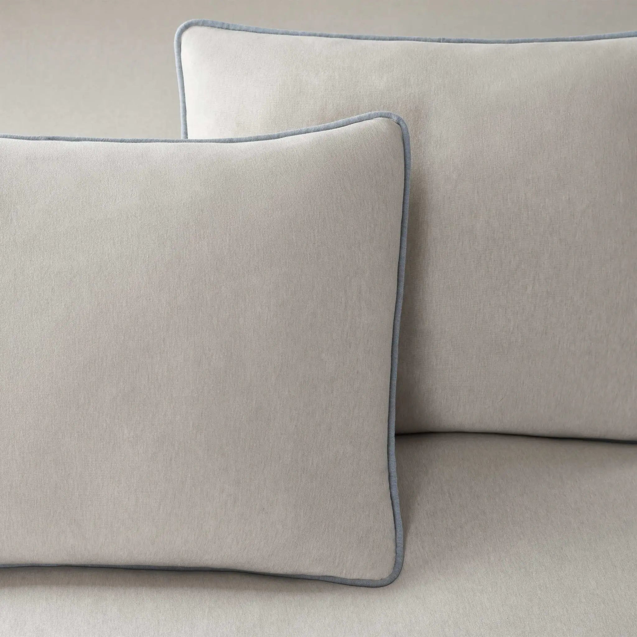 Two gray pillows with blue piping on a beige sofa.