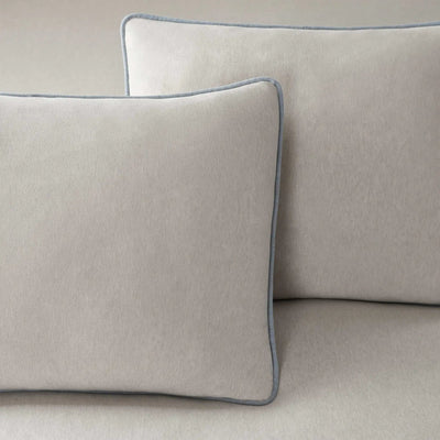 Two gray pillows with blue piping on a beige sofa.