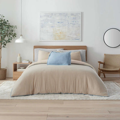 Beige comforter set on a bed in a modern bedroom with abstract art and a chair.