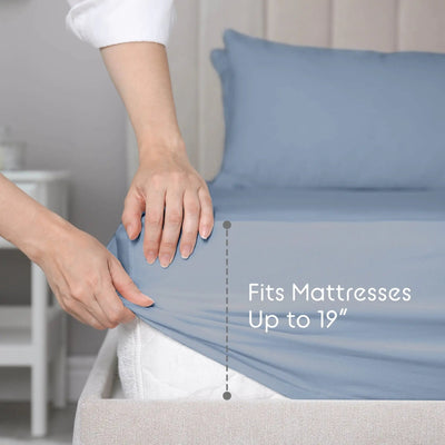 A person's hands stretching a blue fitted sheet over a mattress, demonstrating its stretch. White text on the right reads 'Fits Mattresses Up to 19"' with a vertical dotted line indicating the stretch depth.