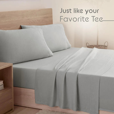 Light gray bedding set including a fitted sheet and two matching pillowcases on a bed with a wooden headboard, with the text 'Just like your Favorite Tee' in the upper right.