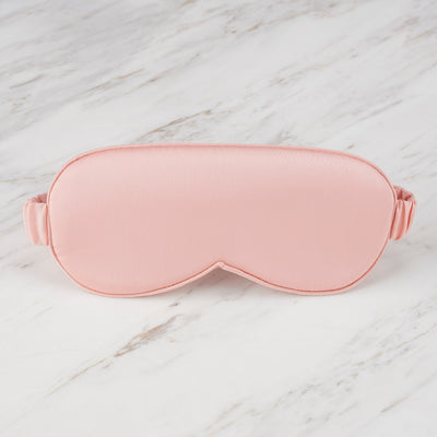 Pink satin eye mask with a soft texture and adjustable strap, placed on a marble surface.