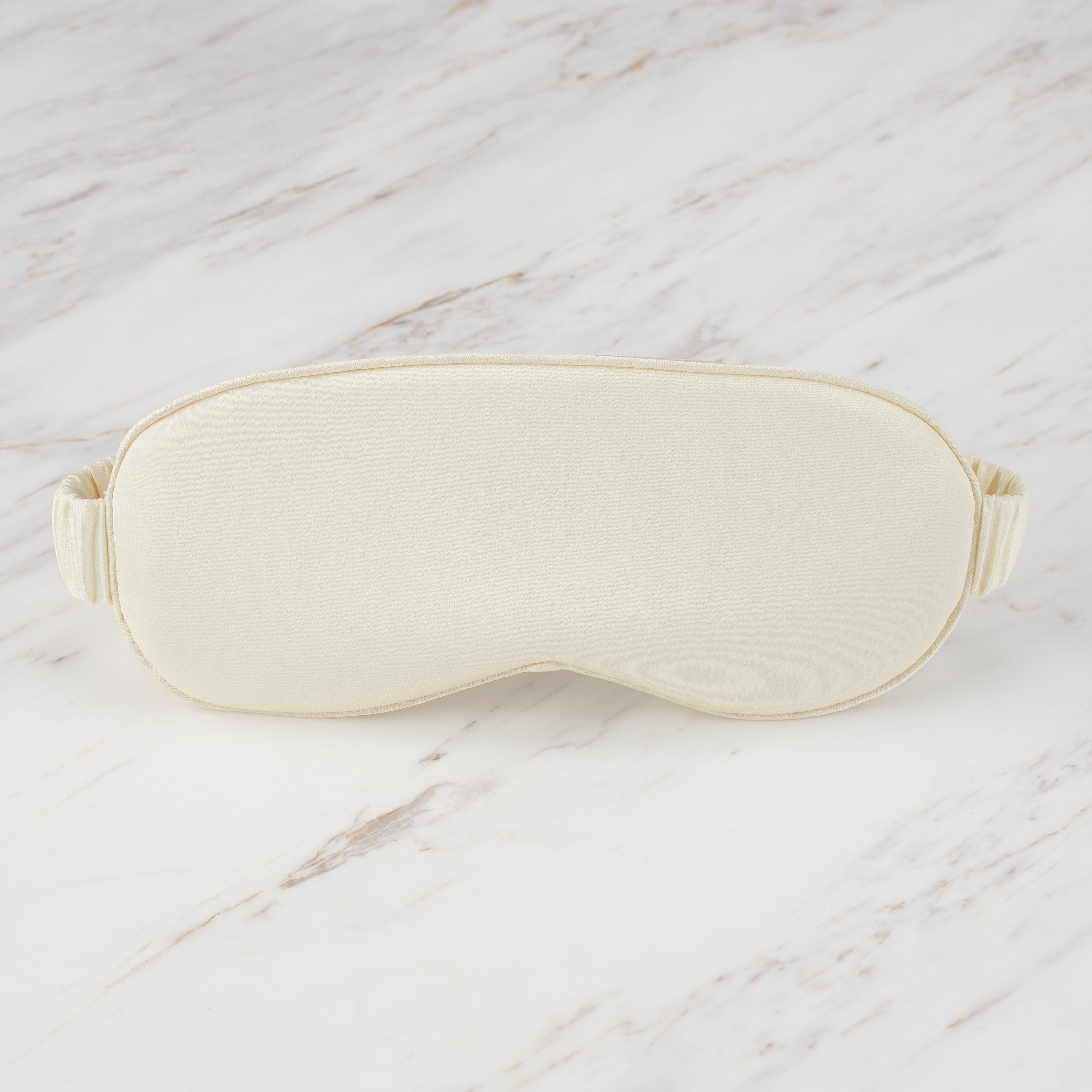 Satin eye mask in a light cream color with an elastic band for a secure fit.