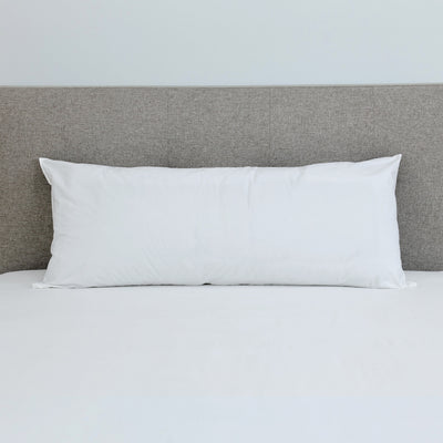 White gusset pillow placed on a bed with a light gray headboard and white bedding.