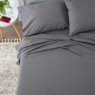 Gray sheet set with two pillows, draped on a bed with a textured rug and a small table nearby.