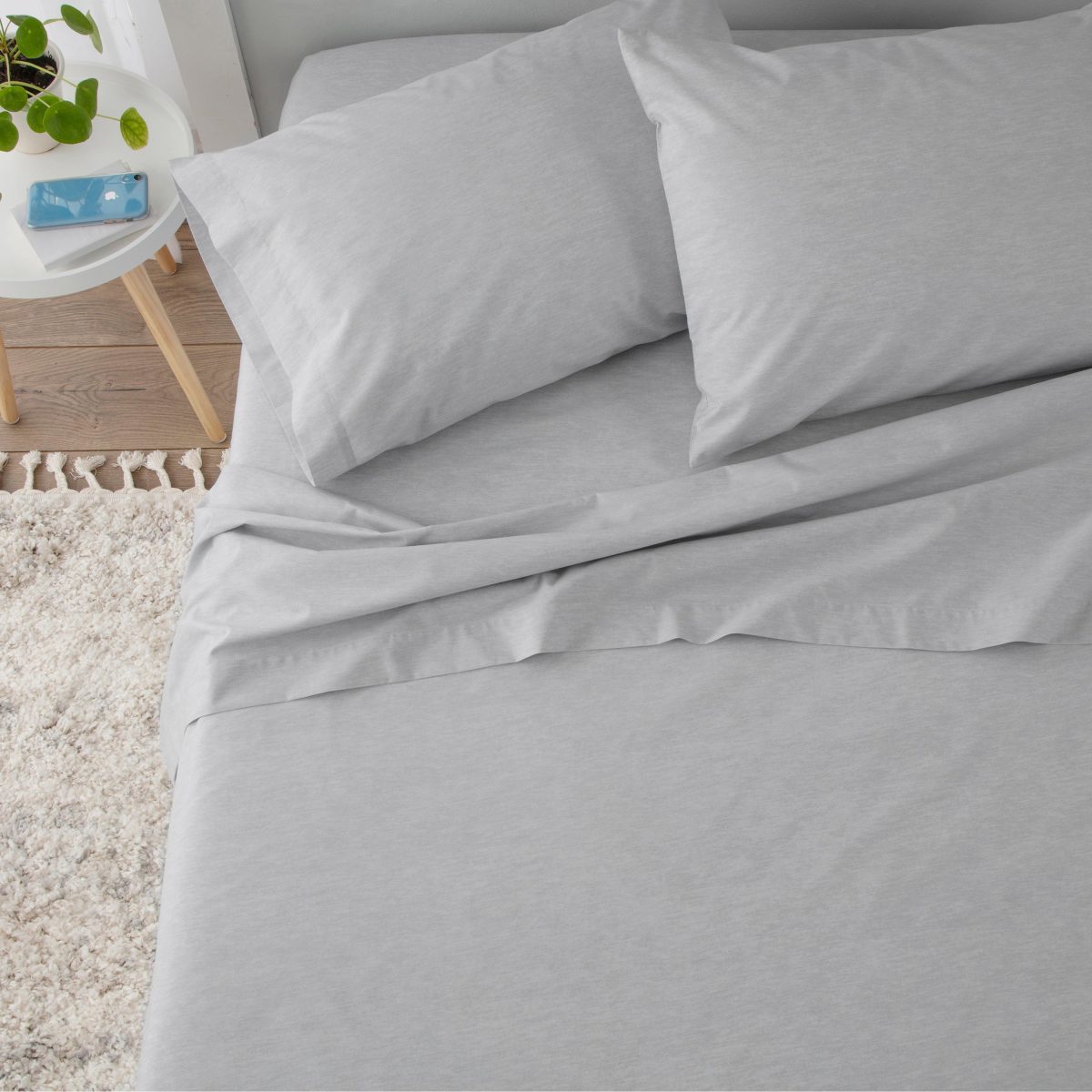 Light gray sheet set with two pillows on a bed, featuring a smooth, flat surface and a textured rug nearby.