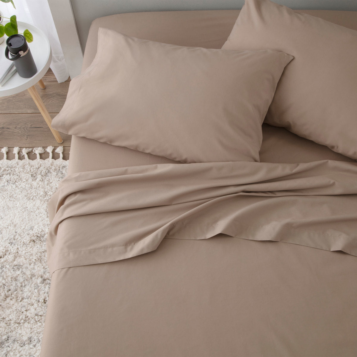 Beige sheet set with two pillows, laid out on a bed with a textured rug nearby.