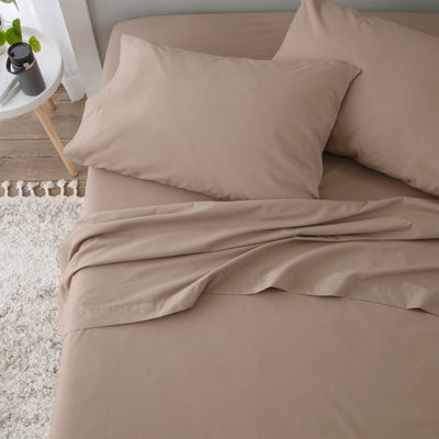Beige sheet set with two pillows, laid out on a bed with a textured rug nearby.