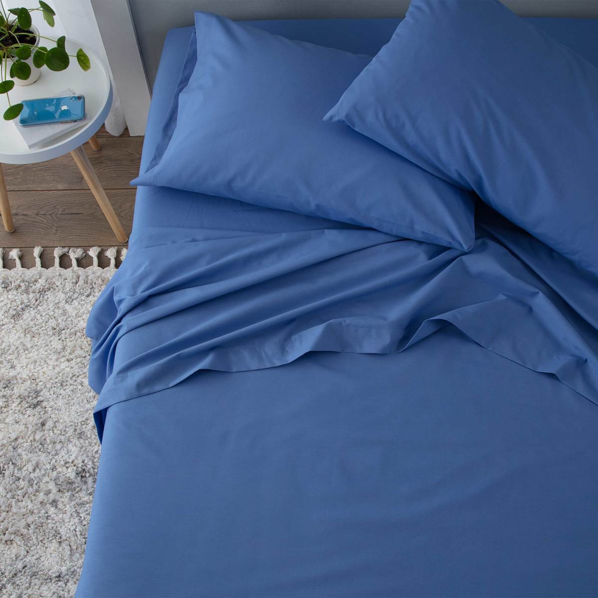Blue sheet set with two pillows, neatly arranged on a bed with a textured rug nearby.
