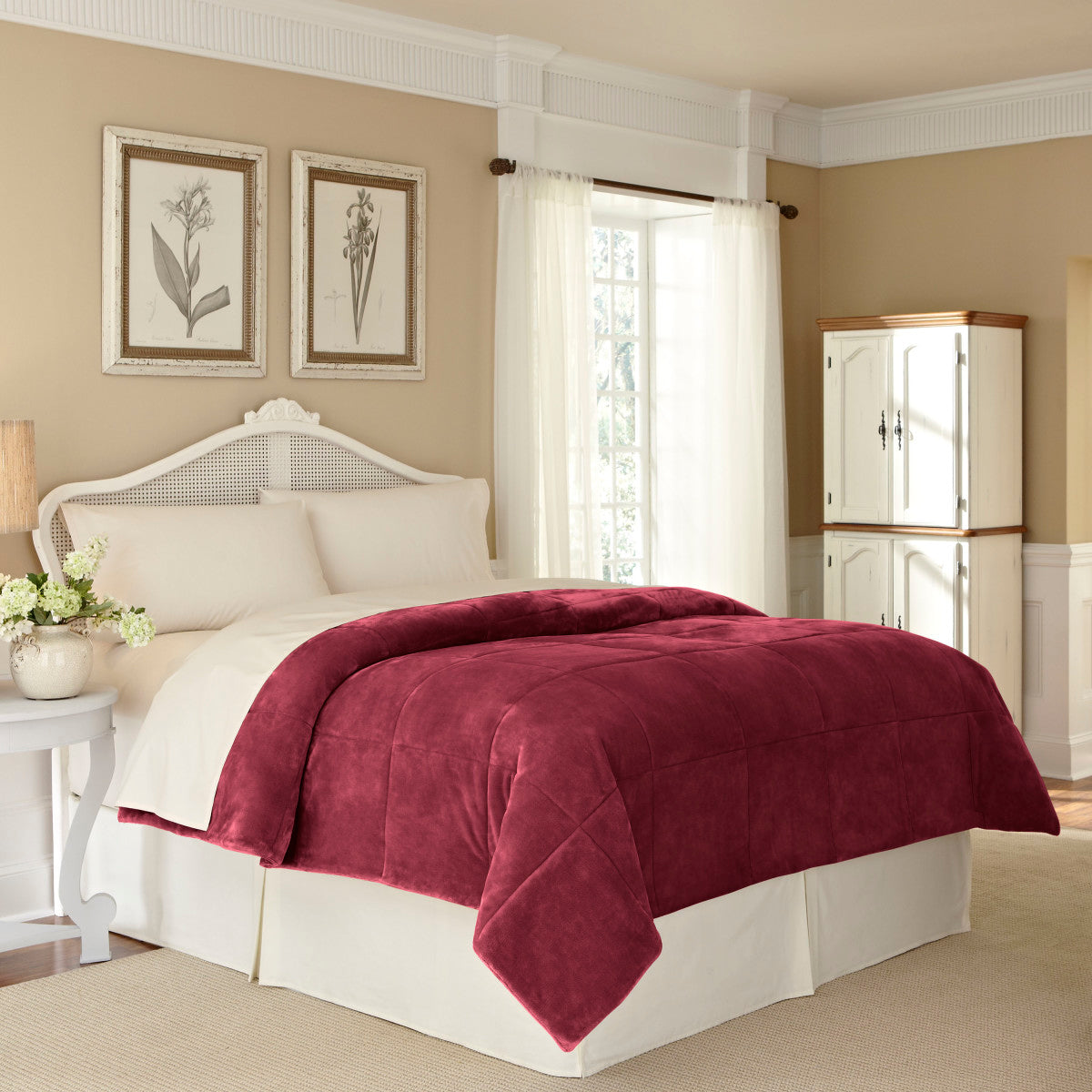 Burgundy plush blanket draped over a bed with white linens in a softly lit bedroom.
