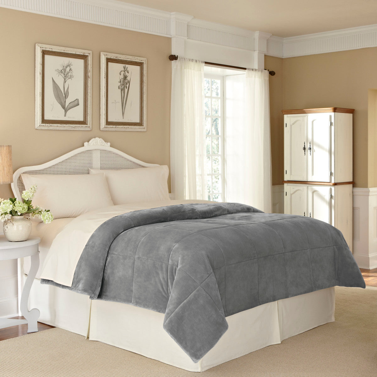 Gray plush blanket draped over a bed with cream-colored bedding in a softly lit bedroom.