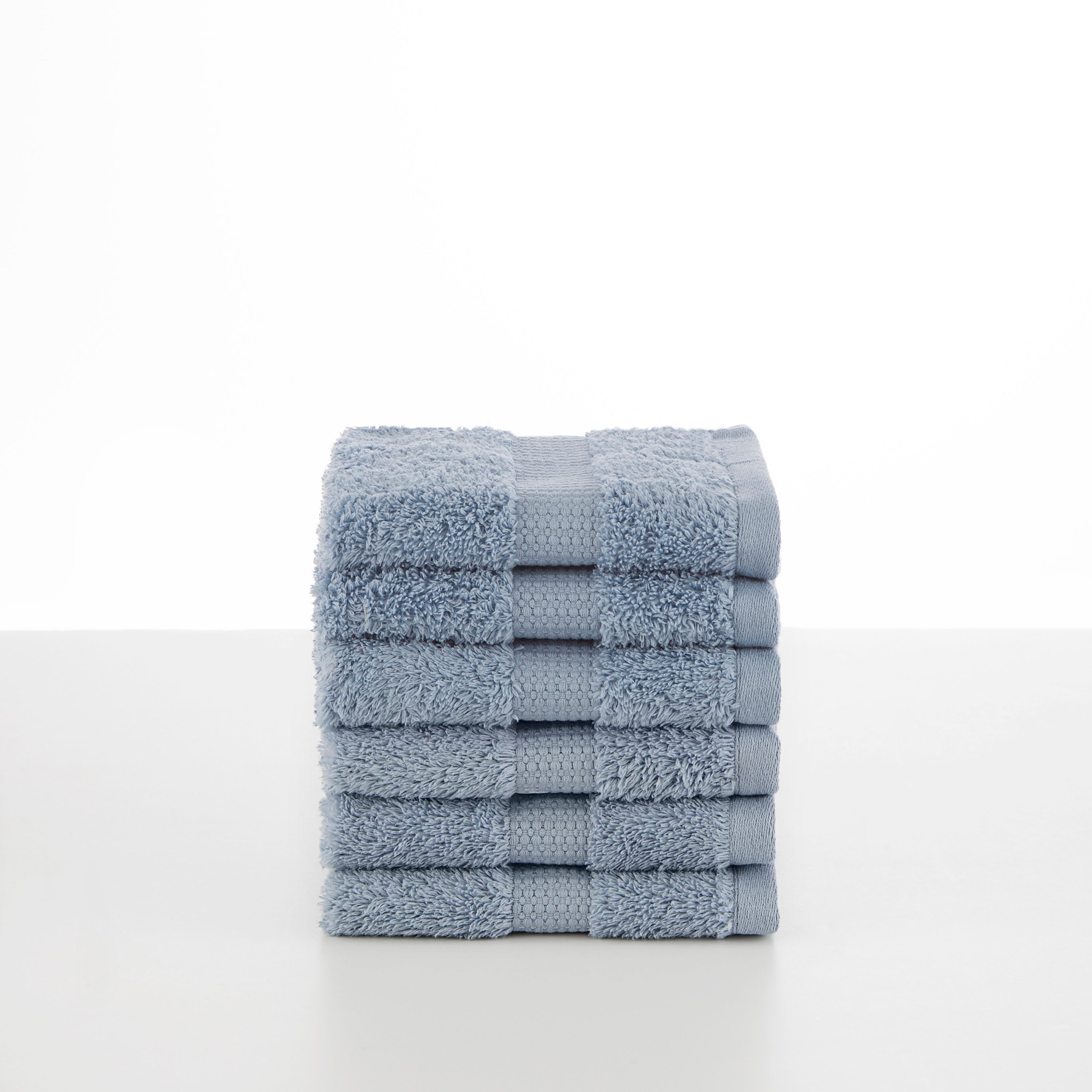 Stack of soft, light blue towels with textured stripes on a white surface.