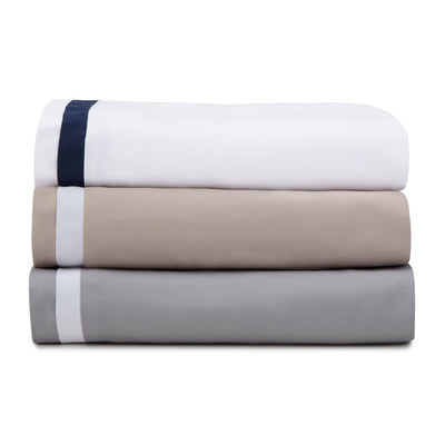 Stack of three folded duvets in white, beige, and gray on a white background