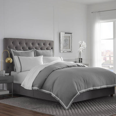 Gray duvet cover set with white trim, paired with matching pillows on a bed with a tufted gray headboard.